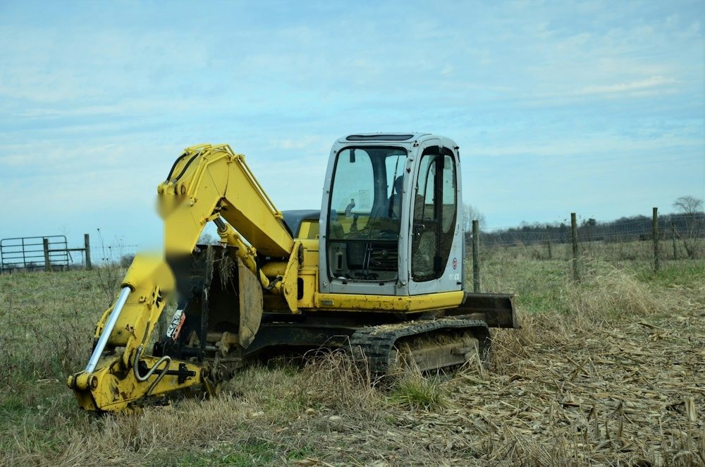 A mini excavator pulling stumps and brush on a partly cleared wooded lot